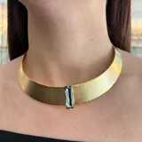 Gargantilla rígida dorada con textura y un cristal Swarovski rectangular en el centro. Cierre con mosquetón y cadena para regular el largo.