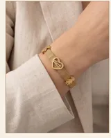 Pulsera de acero con baño de oro, compuesta por una malla metálica flexible y tres dijes pasantes: un corazón con la palabra 'Mamá' grabada, una figura de niña y una figura de niño.