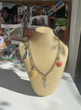 Collar plateado con cadena de eslabones gruesos y dijes colgantes de corazones rojos y amarillos, hojas plateadas y mariposa.