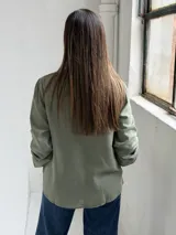 Blusa de color verde oliva con escote en V, cierre frontal con botones y mangas largas con puños elásticos.