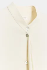 Blusa de viscosa color marfil, con cuello mao, manga larga con puños anchos, cierre frontal con botones y detalle de lazada colgante en el frente.
