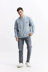 Buzo de algodón color celeste, con cuello redondo, puños y bolsillos laterales. Presenta estampados con texto en el pecho y un parche en la manga.