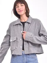 Chaqueta corta gris con cuello camisero, cierre frontal con botones a presión, mangas largas y bolsillos de parche con solapa en el pecho.