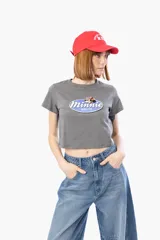 Remera crop top de color gris oscuro con cuello redondo y mangas cortas. Presenta un estampado frontal ovalado con el logo de Minnie Mouse.