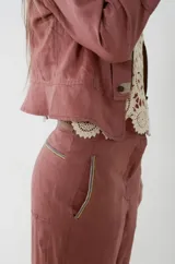 Pantalón sastrero de lino color rosa viejo, de tiro medio con corte flojo en las piernas que se afinan hacia los tobillos. Cuenta con bolsillos frontales con detalles de pasamanería a rayas.