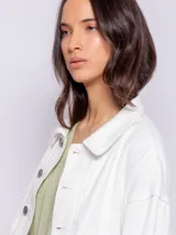 Campera corta de jean color blanco, con cuello camisero, botones metálicos plateados en el frente y puños, y bolsillos delanteros con solapa.