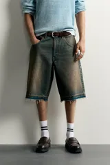 Bermuda de denim de algodón con efecto lavado desgastado en tonos marrones y azules. Tiene tiro medio, diseño de cinco bolsillos, pierna recta de corte holgado y bajo con acabado irregular. Cuenta con cierre frontal de cremallera y botón metálico.