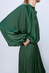 Pantalón de tiro medio confeccionado en tejido satinado verde, con diseño bombacho y bajos acabados en puño elástico. Cuenta con cierre lateral con cremallera oculta en costura.