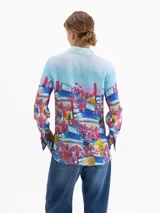 Camisa de seda con cuello clásico, manga larga y cierre frontal con botones ocultos. Presenta un estampado artístico colorido con motivos urbanos y naturales de la cápsula Il Bunny Porta Fortuna.