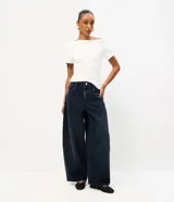 Pantalón barrel de jean color azul oscuro con lavado desgastado, de cintura alta, corte amplio en las piernas y botamanga afinada. Cuenta con cierre frontal y bolsillos funcionales.