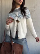Cardigan de tejido de punto con diseño jacquard en la parte superior, cuello redondo y cierre frontal con botones. Presenta un patrón geométrico en tonos gris y azul sobre base color crema.