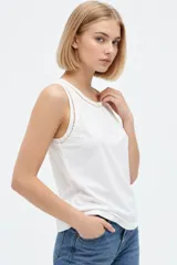 Musculosa blanca de algodón, de corte ajustado, con cuello redondo y detalles de broderie en los bordes.