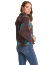 Camisa de crepe marca ABS Allen Schwartz, color marrón con estampado de hojas en tonos verdes y azules. Presenta cuello con solapa, cierre frontal con botones, mangas largas anchas y detalle de bordado con mostacillas en los hombros.