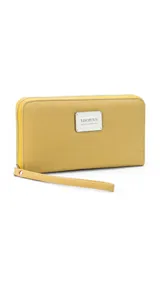 Billetera larga con cierre perimetral, confeccionada en material sintético texturizado color mostaza. Cuenta con correa de mano extraíble y placa metálica con logo de la marca en el frente.