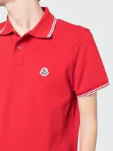 Remera polo Moncler confeccionada en piqué de algodón color rojo, con cuello y puños acanalados con líneas blancas y detalle de parche con logo en el pecho.