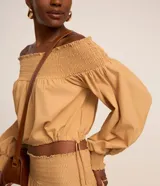 Blusa color ocre de tricolina con escote hombro a hombro con lastex, mangas largas con lastex en los puños y regulador en la parte baja.