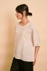 Blusa holgada color beige con mangas cortas y cuello redondo. Presenta apliques bordados con detalles de perlas y lentejuelas en el frente.