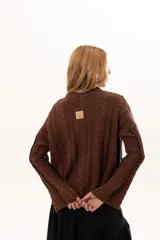 Buzo de tejido de punto color chocolate con diseño de trenzas verticales y detalles de costuras en contraste color negro. Presenta cuello redondo, mangas largas con terminación acampanada y aberturas laterales en el ruedo.