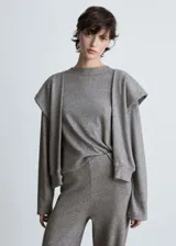 Buzo de punto fino color gris melange, con cuello redondo y diseño de mangas con solapas decorativas superpuestas. Presenta un corte recto y mangas largas con puños ajustados.