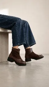 Bota corta de cuero color marrón, con diseño de texturas combinadas, talón con textura grabada, taco geométrico y cierre lateral.