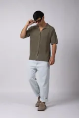 Camisa de punto calado en color beige, de manga corta y corte relajado. Presenta cuello tipo bowling, cierre frontal con botones al tono y una estructura liviana y respirable confeccionada en algodón.