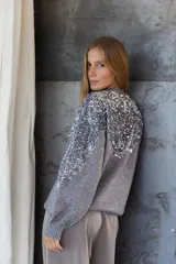 Buzo de punto color gris con diseño holgado, cuello redondo y detalle de lentejuelas plateadas en la parte frontal superior y hombros.