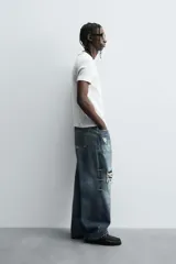 Camiseta de corte relajado, color gris claro, confeccionada en tejido con estructura waffle. Presenta cuello redondo y manga corta, con costuras decorativas en contraste color dorado que recorren los laterales y los hombros.