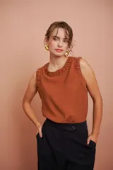 Blusa sin mangas color terracota, con escote redondo y detalles fruncidos en el cuello y las sisas.