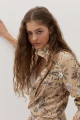 Camisa beige de manga larga, con cuello camisero, cierre frontal con botones y un estampado detallado de motivos botánicos e insectos en tonos oscuros.
