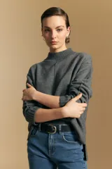 Polera de tejido de punto color gris, con cuello alto acanalado, hombros caídos y costura central decorativa en el frente. Presenta un diseño holgado con terminaciones acanaladas en puños y ruedo.