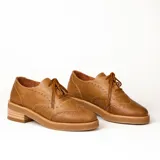 Zapato acordonado estilo oxford de cuero vacuno en color plateado metalizado, con diseño brogue, suela de goma y taco de madera.