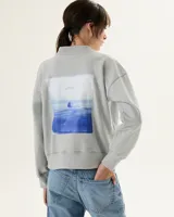 Buzo gris claro de algodón con cuello medio y estampa rectangular con diseño de paisaje marítimo en tonos azules.