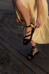 Sandalias bajas de cuero color marrón, con tiras finas para atar alrededor del tobillo.