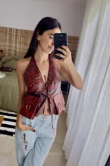 Chaleco top de cuero con efecto desgastado, escote halter profundo y cierre frontal con múltiples tiras para atar. Presenta bolsillos frontales aplicados con detalles de argollas metálicas.