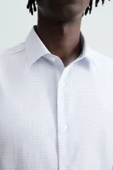 Camisa de manga larga para hombre, corte slim fit, con cuello italiano y cierre frontal de botonadura. Presenta un microestampado de cuadros pequeños en tonos blanco y celeste.