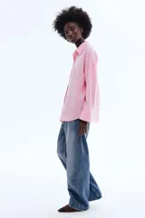 Camisa de corte oversized en tejido liviano de lino y viscosa, de color rosado. Cuenta con cuello clásico, cierre frontal de botones, hombros caídos y mangas largas con puños abotonados. El diseño se completa con un bajo redondeado.