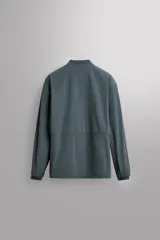 Chaqueta técnica de corte relajado, confeccionada en tejido compacto y elástico. Presenta cuello y puños acabados en rib, cierre frontal con cremallera, bolsillos frontales con cremallera oculta y bajo ajustable con elástico en los laterales.