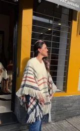 Poncho de lana merino tejido en telar de peine, color marfil con diseño a cuadros en tonos azul marino y rojo, terminado con flecos en el ruedo.