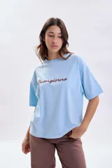 Remera de corte boxy color celeste, con mangas cortas y cuello redondo. Presenta la palabra 'Buongiorno' bordada en el frente en color marrón.