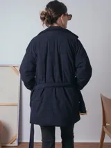 Campera de pana color marrón, con diseño acolchado, cuello camisero, cierre frontal oculto y cinturón ajustable con hebilla a tono. Presenta bolsillos frontales con solapa y mangas largas de corte holgado.