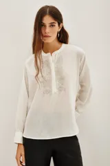 Camisa de algodón color blanco, con cuello redondo, cierre frontal parcial con botones y detalle de bordado con canutillos en el frente.