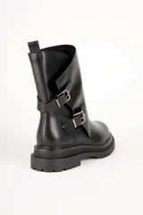 Bota de caña media color negro, de estilo biker, con suela chunky y dos tiras con hebillas metálicas en el lateral.