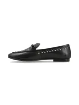 Mocasín de cuero negro con tachas metálicas decorativas a lo largo del borde y en la lengüeta, con tira frontal y hebilla metálica.