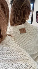 Poncho tejido en lana merino color crudo, con cuello alto y etiqueta de cuero con logo en la espalda.