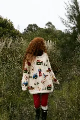 Buzo tejido de lana merino color crema, con diseño bordado a mano que representa escenas de granja, incluyendo figuras de granjeros, casas, tractores y animales. Presenta un corte holgado y cuello redondo.