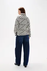 Sweater de tejido jacquard con diseño geométrico de líneas entrelazadas en tonos negro y marrón. Presenta cuello alto, mangas largas con terminación holgada y un corte recto.