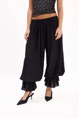 Pantalón negro de corte amplio, con cintura elástica fruncida y diseño abombacho con volados en los tobillos.