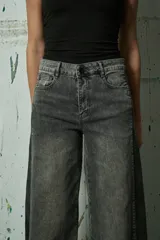 Jean de corte wide leg en color gris lavado, con diseño bicolor que presenta un panel lateral en un tono de gris más oscuro. Posee tiro medio, cierre frontal con botón y bolsillos laterales.