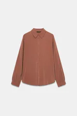 Camisa celeste de manga larga con cuello solapa y pliegues en los puños. Presenta cierre frontal con botones forrados al tono y bajo asimétrico.