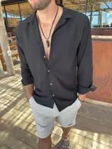 Camisa de manga larga color negro, confeccionada en tela liviana y fresca, con cuello clásico y botones frontales en contraste.